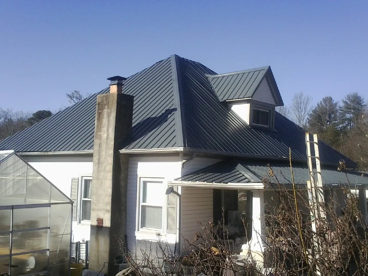Dark blue standing seam metal roof on a white farmhouse with dormer — Slate & Tile Roof Repair by Roofing Brothers in Astor