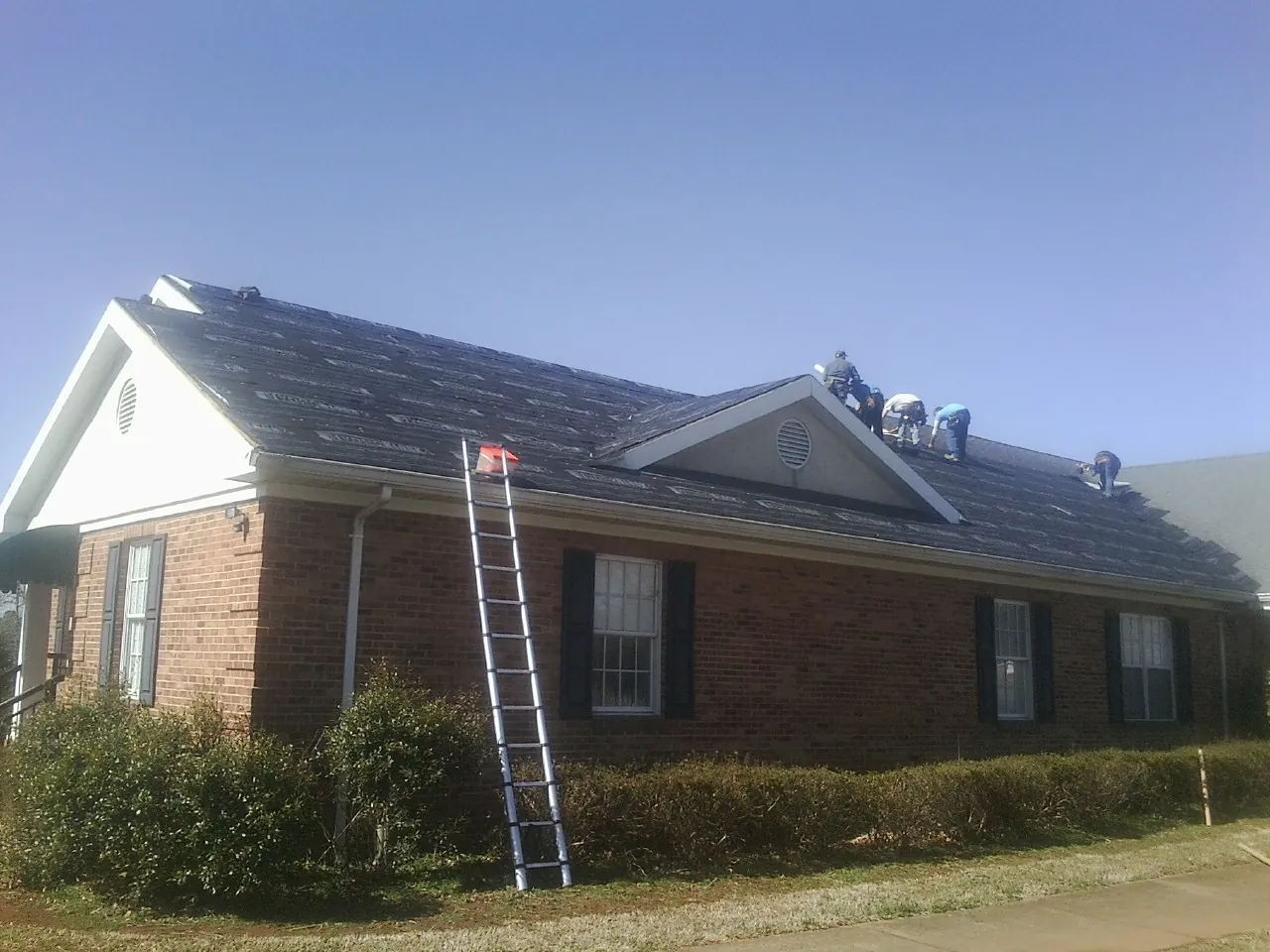 Crew tearing shingles off a brick ranch roof with a ladder set — Metal Roof Repair work by our crew in Astor