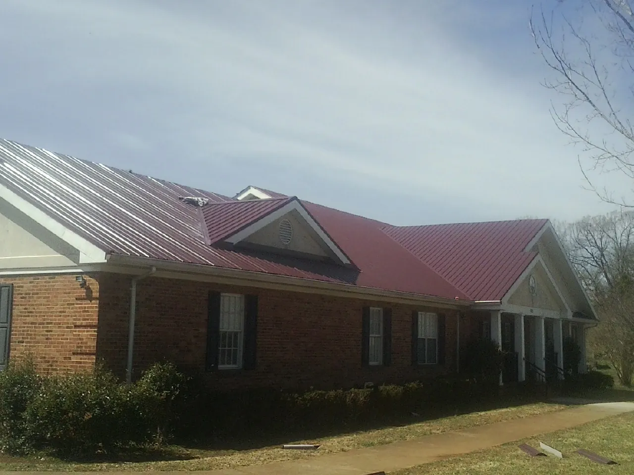 Red metal roof with gabled entries on a long brick building, from a Hail Damage Roof Repair job in Astor
