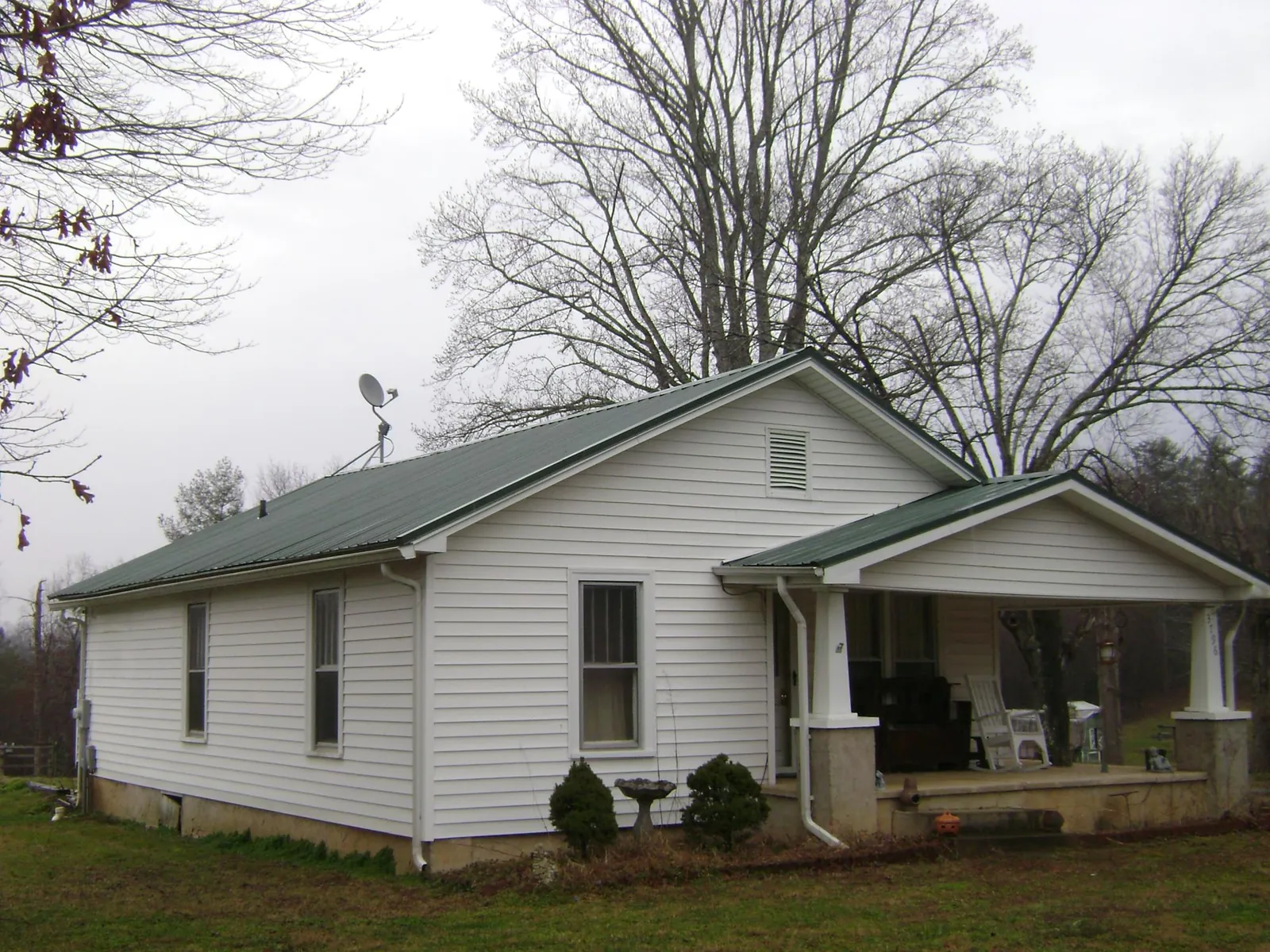 Green metal roof on a white bungalow with a side porch in Astor