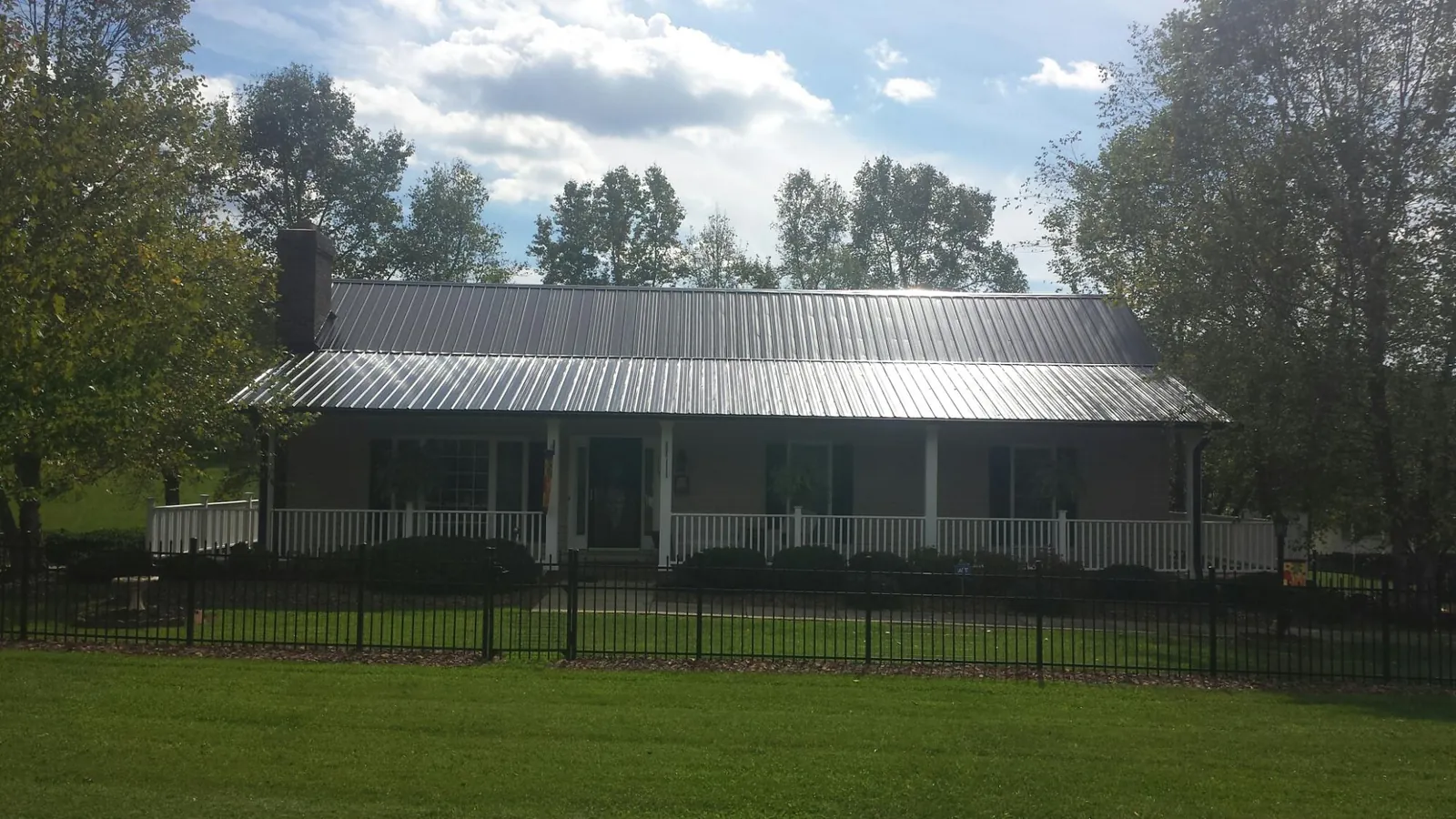Gray metal roof on a brick ranch with a full width front porch — Gutter Guard Installation work by our crew in Astor