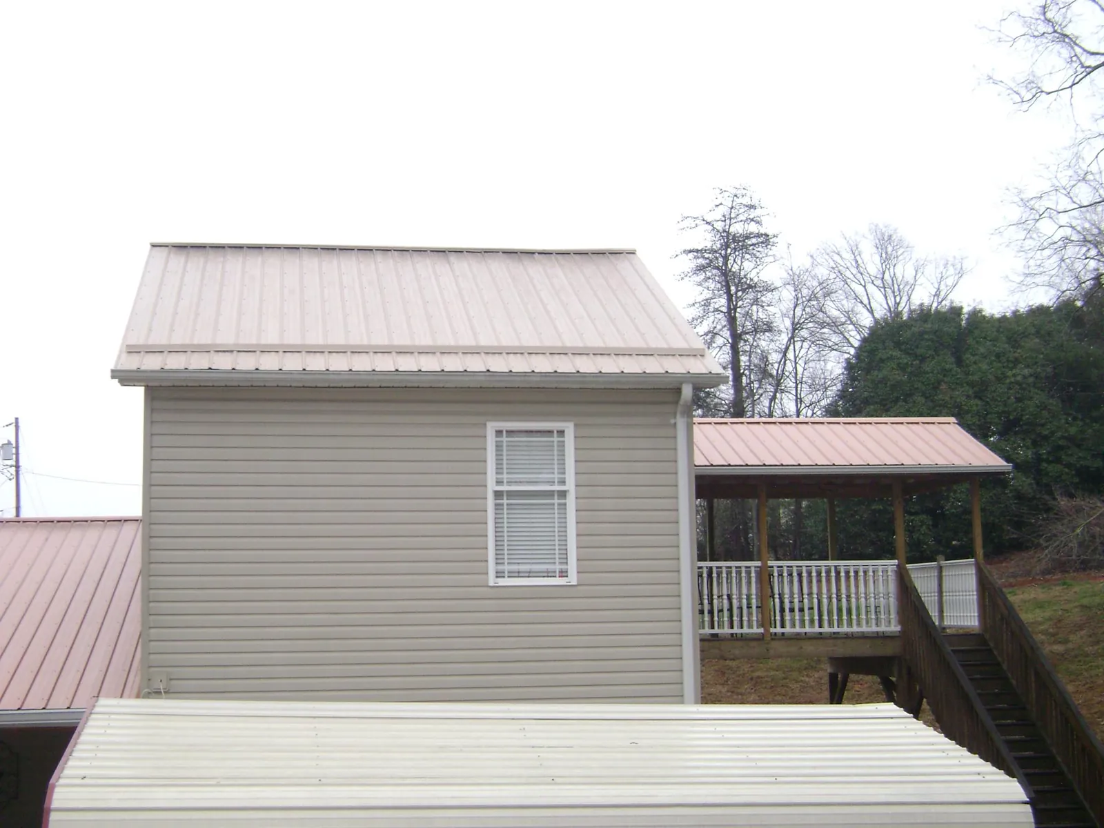 Tan metal roofs on a two story addition and attached porch, from a Roof Replacement job in Astor
